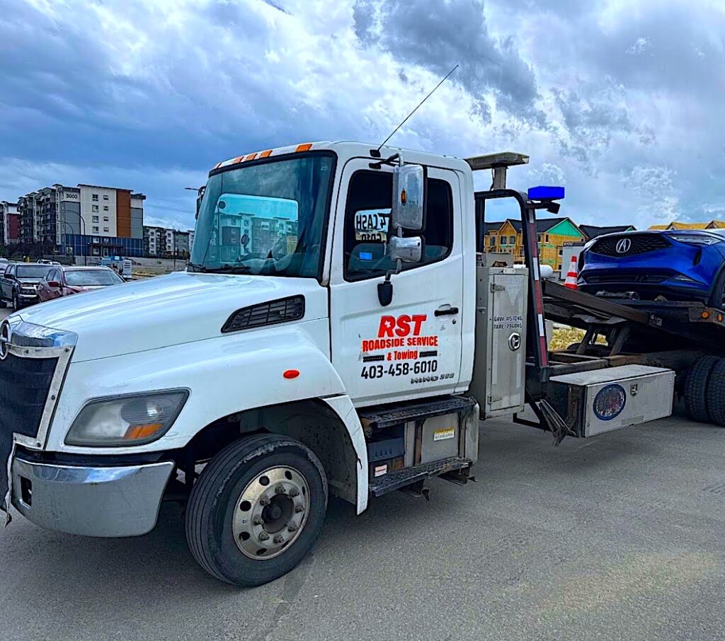 RST Towing's flatbed tow truck is loading a car on the bed.
